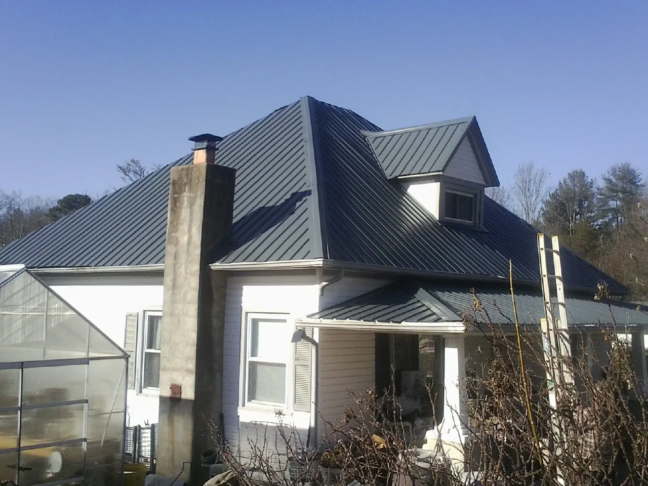 Dark blue standing seam metal roof on a white farmhouse with dormer — Slate & Tile Roof Repair by Roofing Brothers in Durhamville