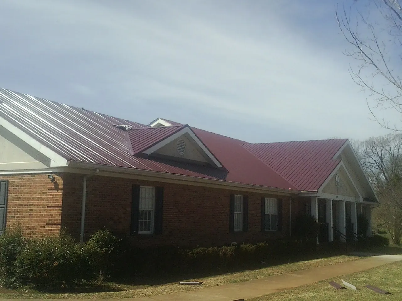 Red metal roof with gabled entries on a long brick building, from a Hail Damage Roof Repair job in Durhamville