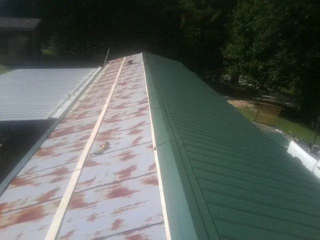 Old rusted panels beside newly installed green metal roofing — Wind Damage Roof Repair by Roofing Brothers in Durhamville