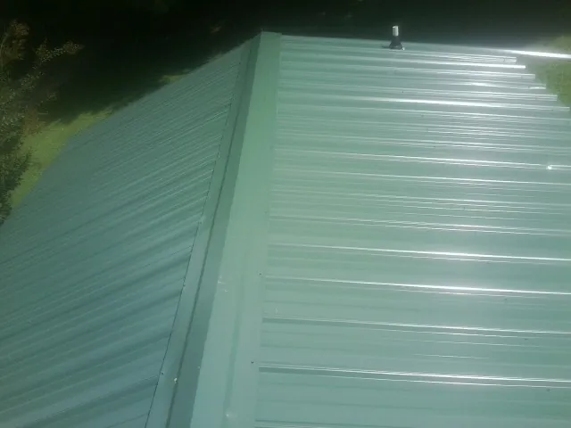 New green metal panels meeting at the ridge of a roof — Flat Roof Repair work by our crew in Durhamville