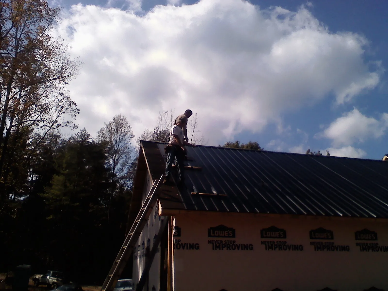Roofer fastening dark metal panels high against a cloudy sky, from a Roof Inspection job in Durhamville