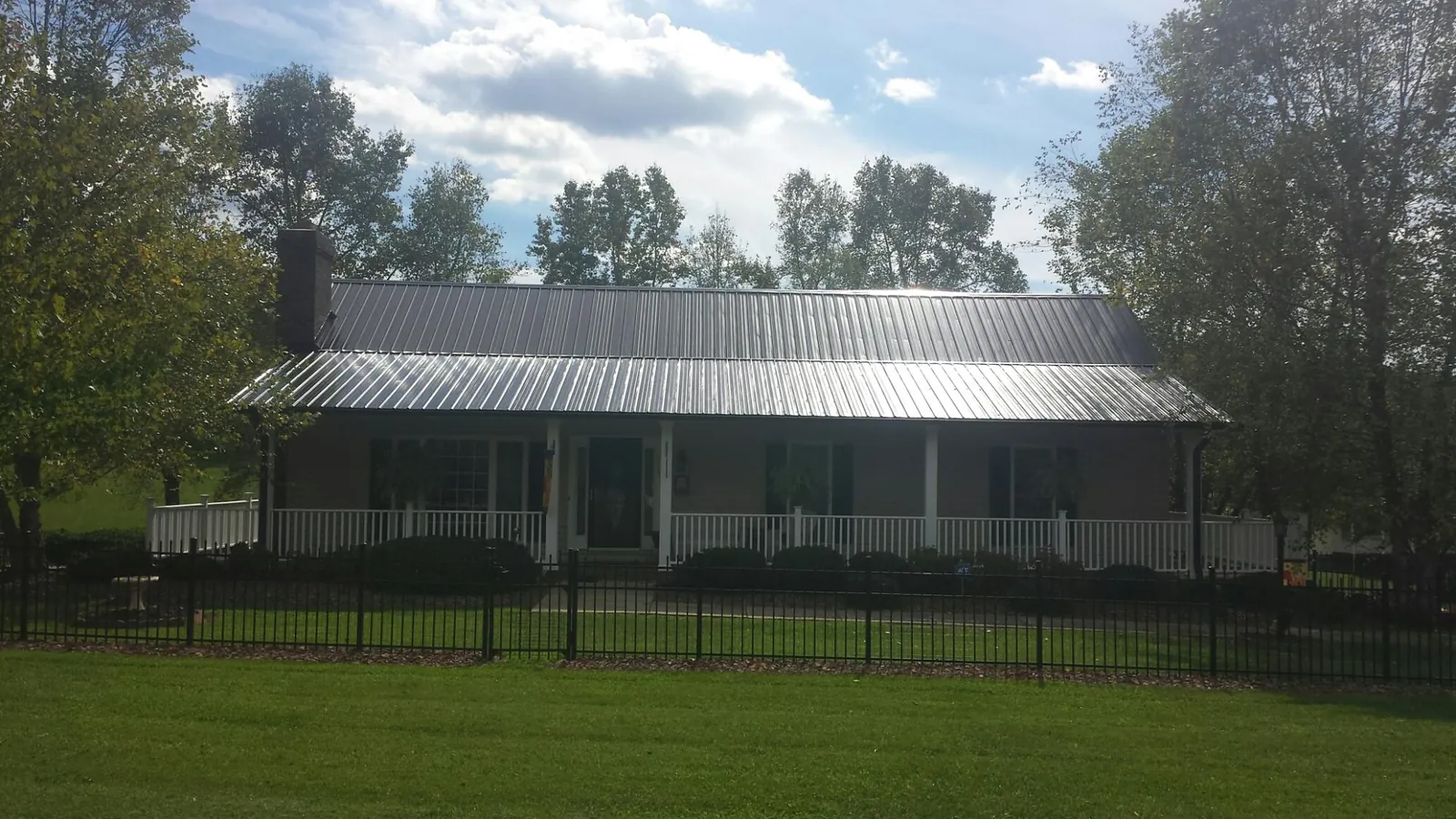 Gray metal roof on a brick ranch with a full width front porch — Gutter Guard Installation work by our crew in Durhamville
