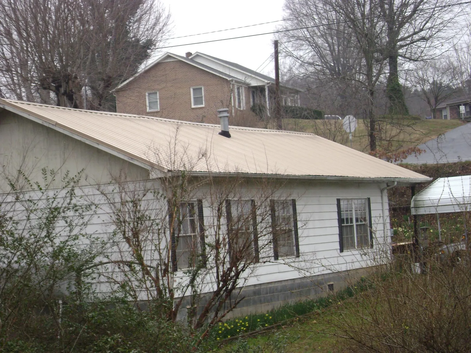 Tan metal roof on a white sided house set into a hillside — Commercial Roofing by Roofing Brothers in Durhamville