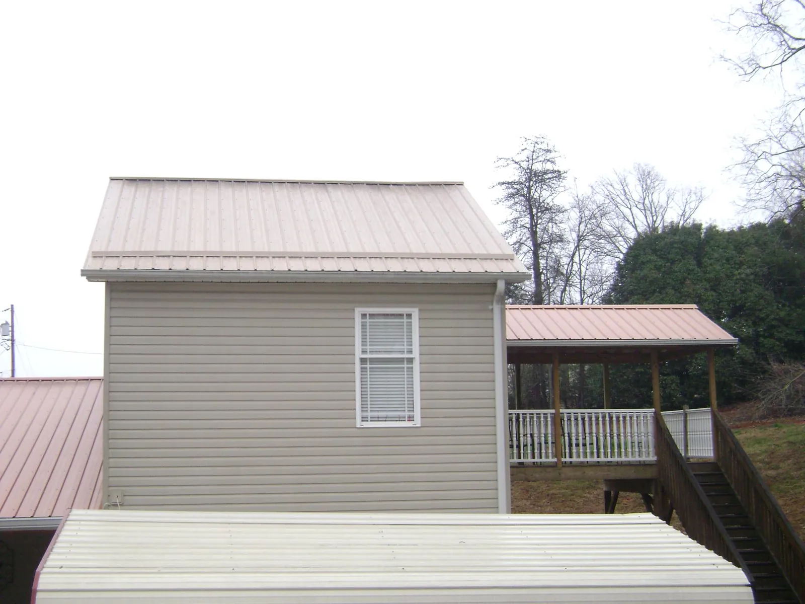 Tan metal roofs on a two story addition and attached porch, from a Roof Replacement job in Durhamville